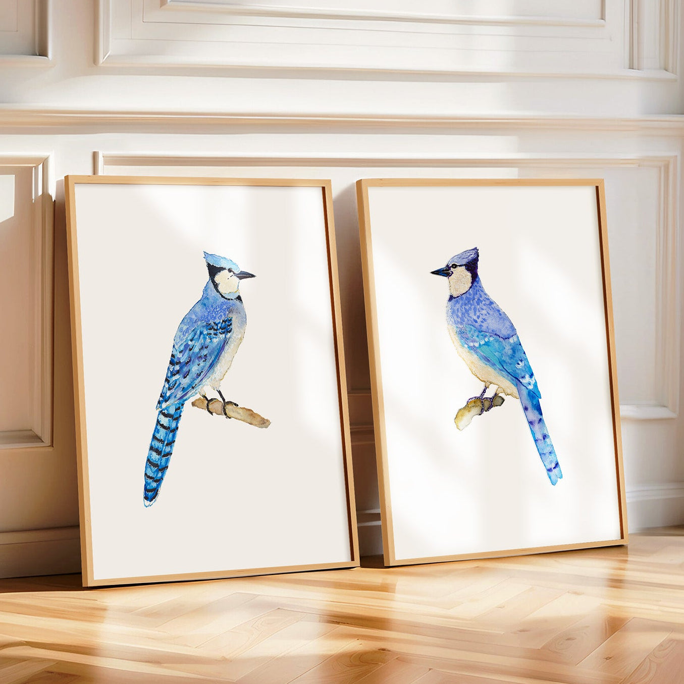 Two framed prints of blue birds on a wooden floor with a plant and decorative wall.
