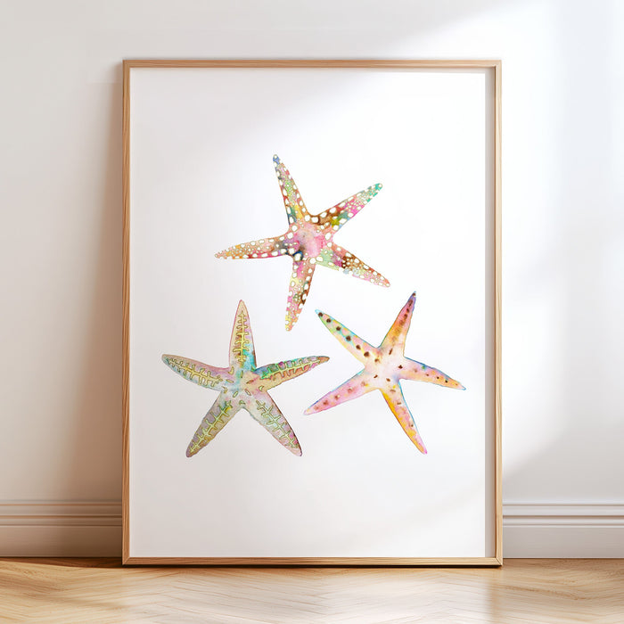 A framed art print featuring a watercolor painting of three colorful starfish on a white background, displayed in a room setting.